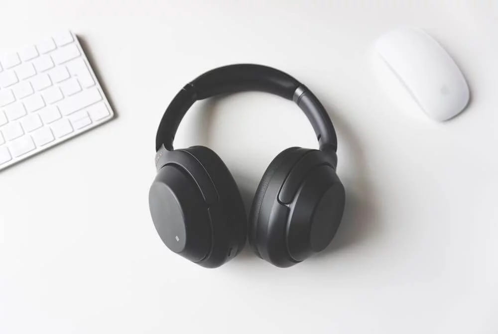 Black over-ear headphones on a white desk between a keyboard and a mouse