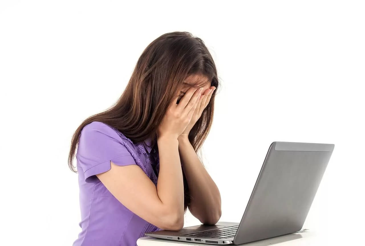 A woman covering her face with her hands beside an open laptop