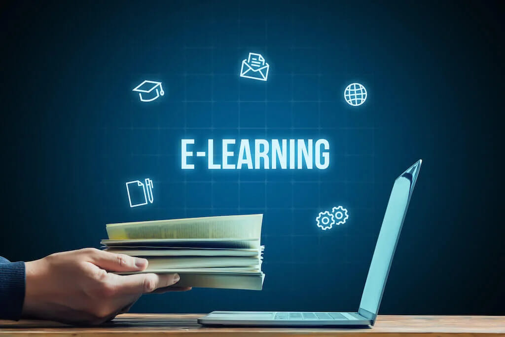 Напис e-learning на темному тлі з піктограмами, поряд рука кладе книжки біля ноутбука