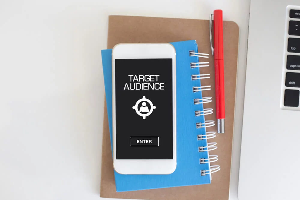 A phone lying on a notebook, its screen showing the words target audience above an Enter button
