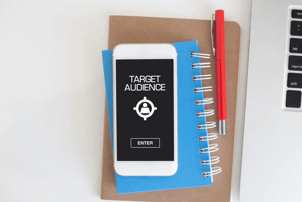 A phone lying on a notebook, its screen showing the words target audience above an Enter button