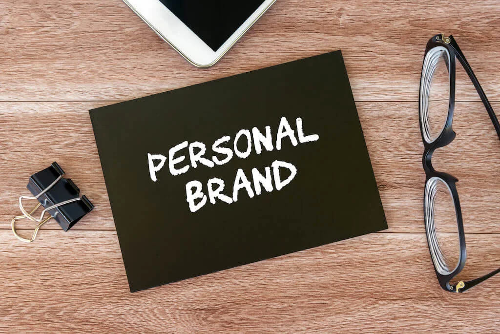 Темна картка з написом personal brand на столі поруч з окулярами і планшетом