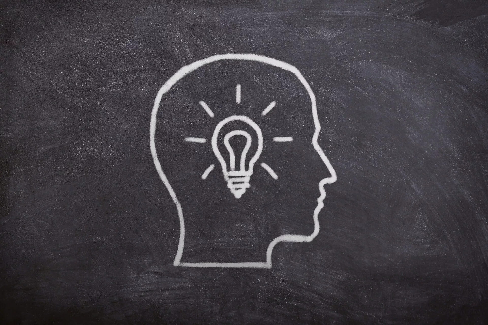 A chalk drawing of a head in profile with a lit bulb where the brain would be