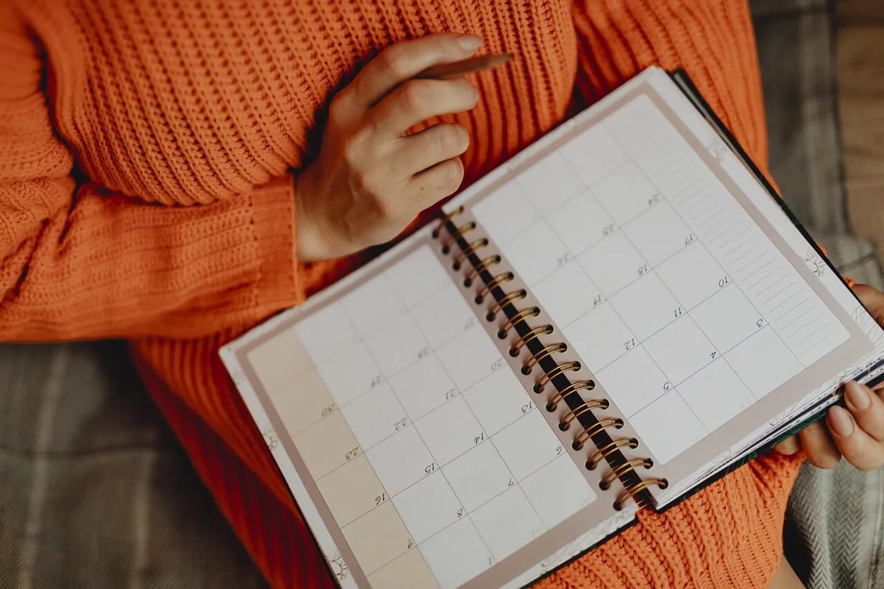 Hands in an orange jumper holding an open blank weekly planner