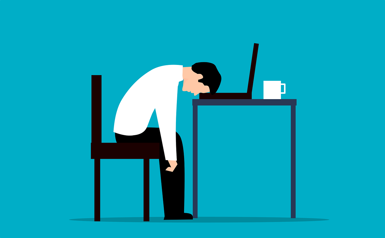 A flat illustration of a person slumped face down on a desk next to a laptop and a mug