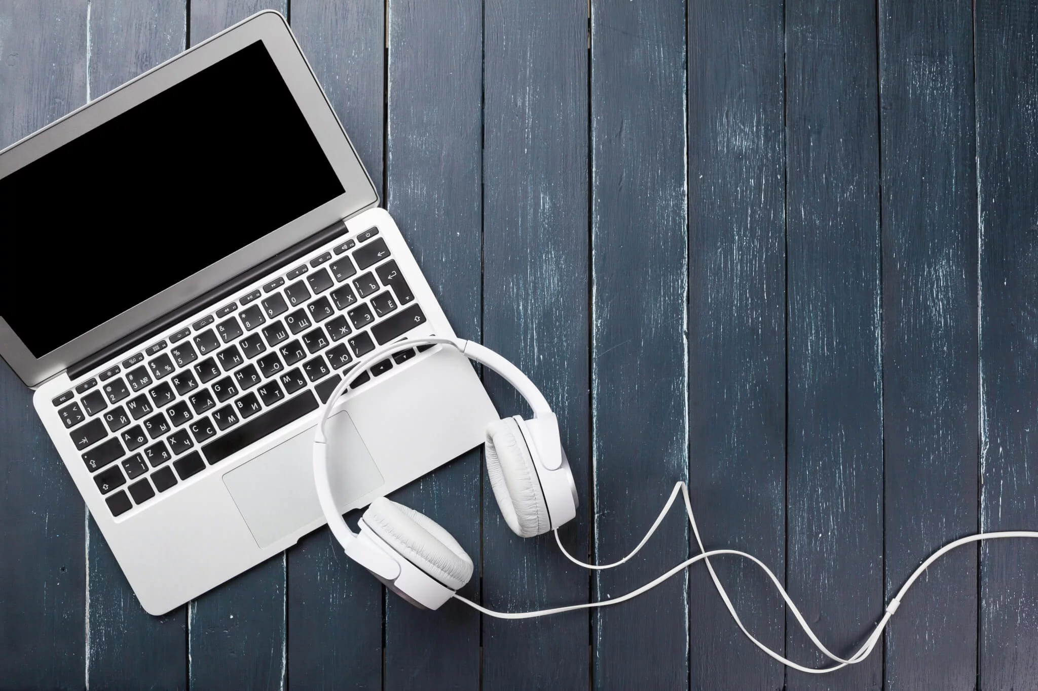 A laptop and white headphones lying on a dark wooden desk