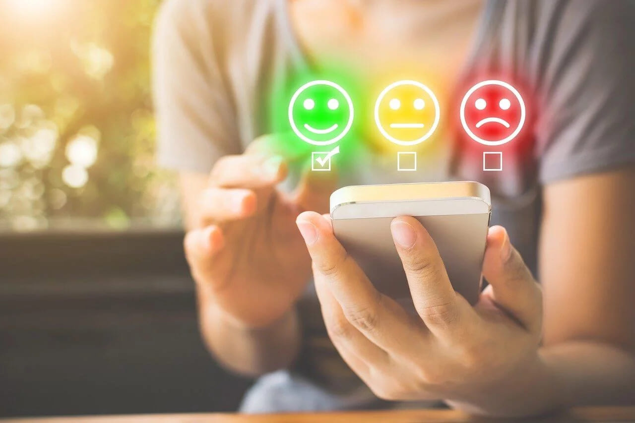 A hand tapping a green smiling face on a phone in a three-way emoji rating