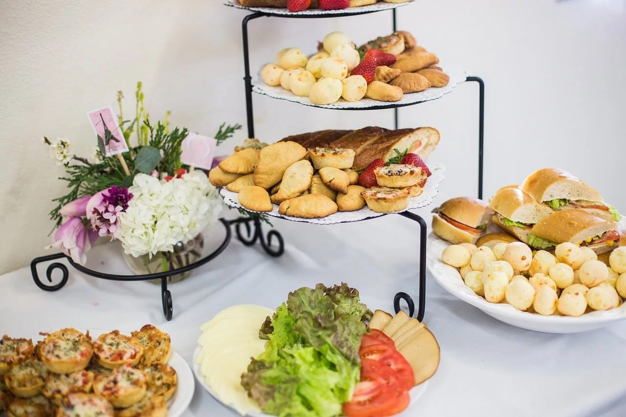 A catering table with tiered stands of pastries, sandwiches and mini quiches beside a vase of flowers