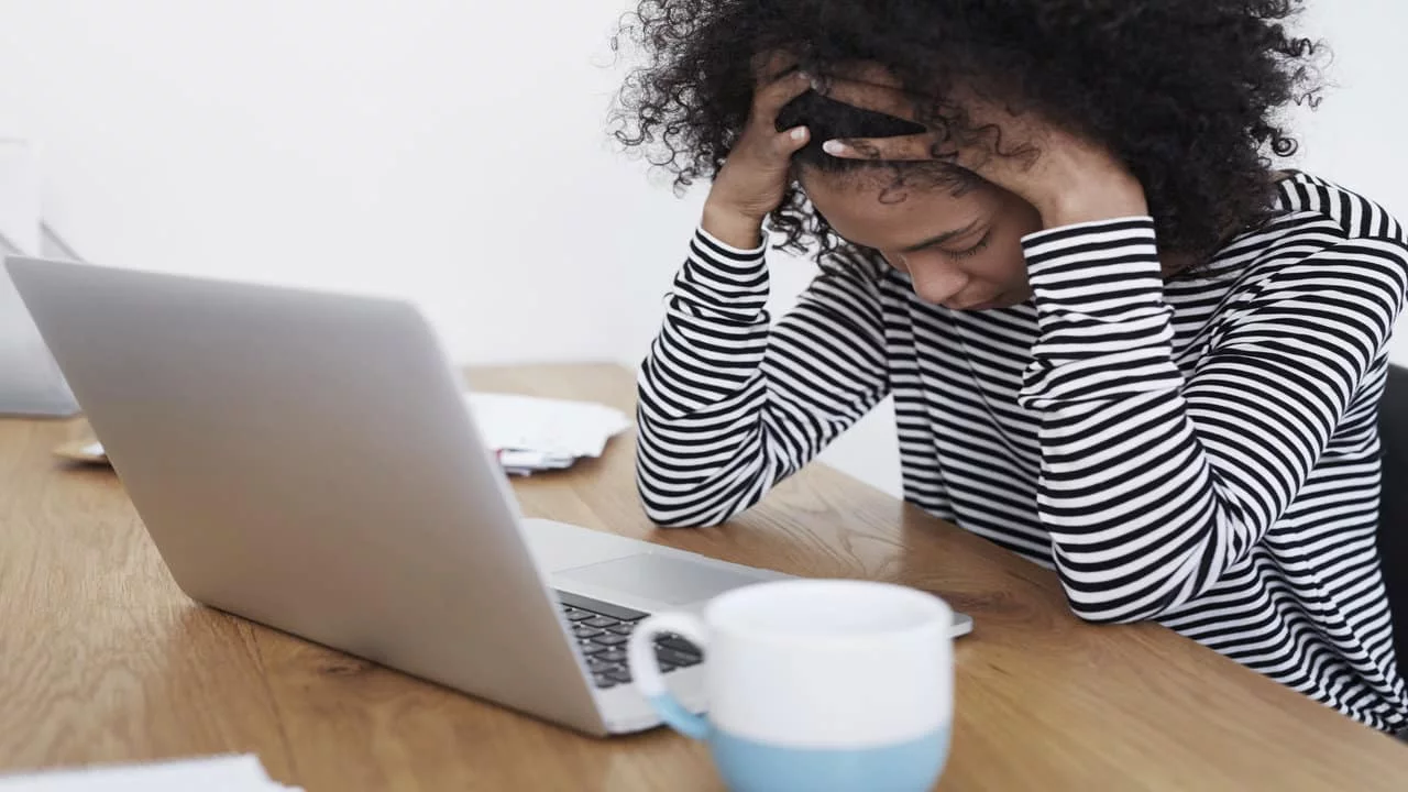 Stressed woman sitting at a desk with laptop, frustrated by a failed webinar or technical error