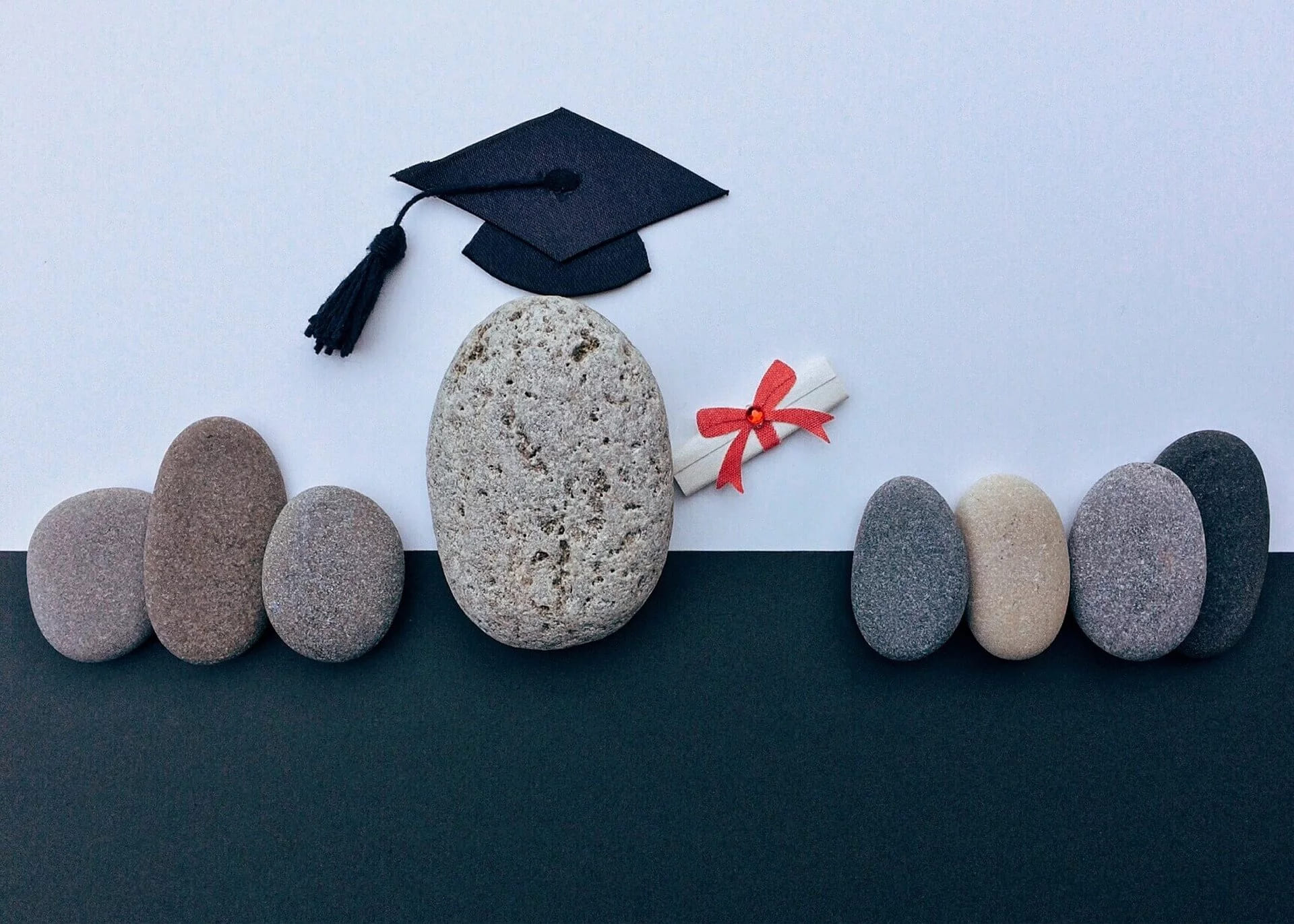 A graduation cap and a tied diploma resting on a row of stones