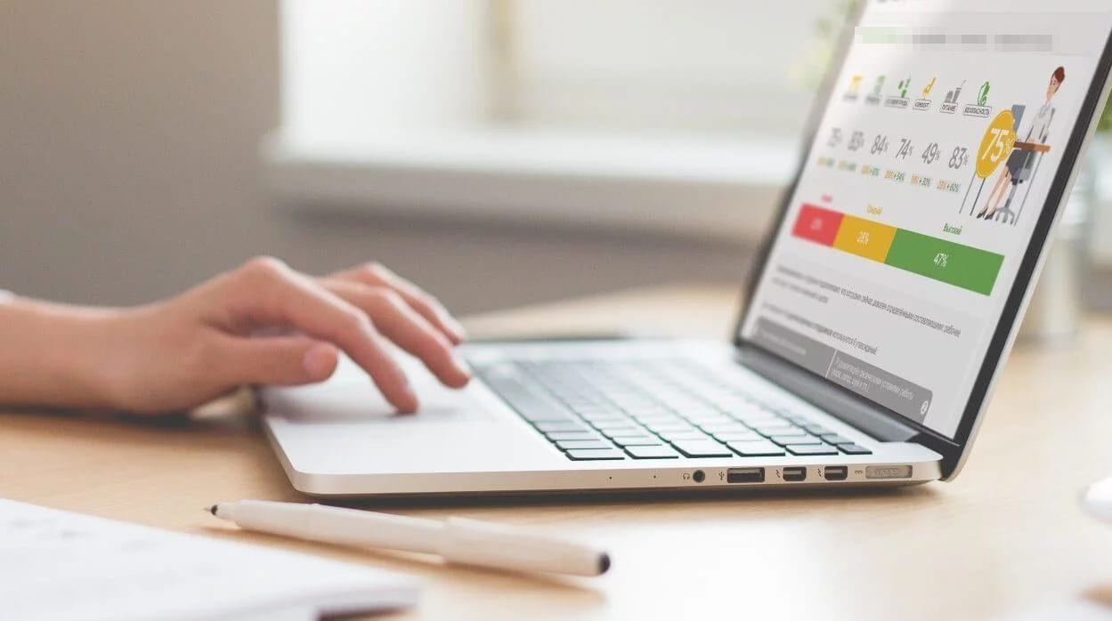 Hands typing on a laptop whose screen shows a survey results dashboard with percentages and a red, yellow and green bar