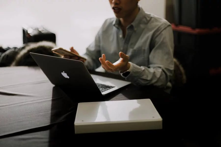 A man gesturing as he speaks in front of an open laptop