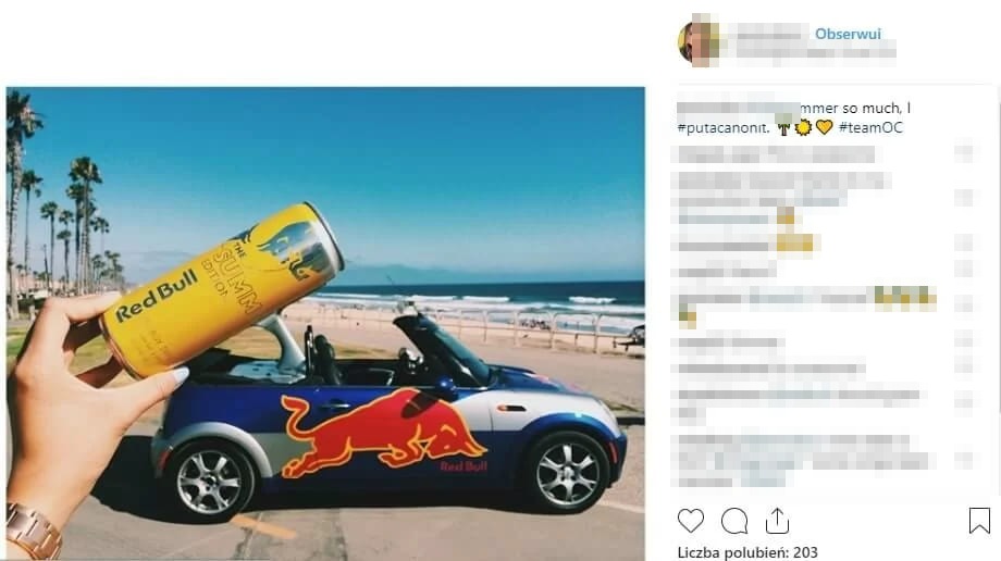 Post na Instagramie ze zdjęciem ręki trzymającej puszkę Red Bull na tle samochodu Red Bull przy plaży z palmami, z hasztagiem #putacanonit i rozmytym podpisem