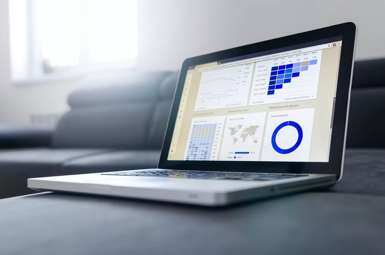 A laptop on a sofa showing a dashboard of charts and a world map