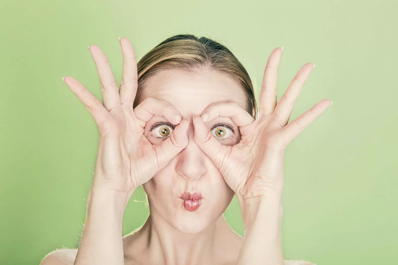 A woman making binoculars with her fingers, eyes wide in surprise