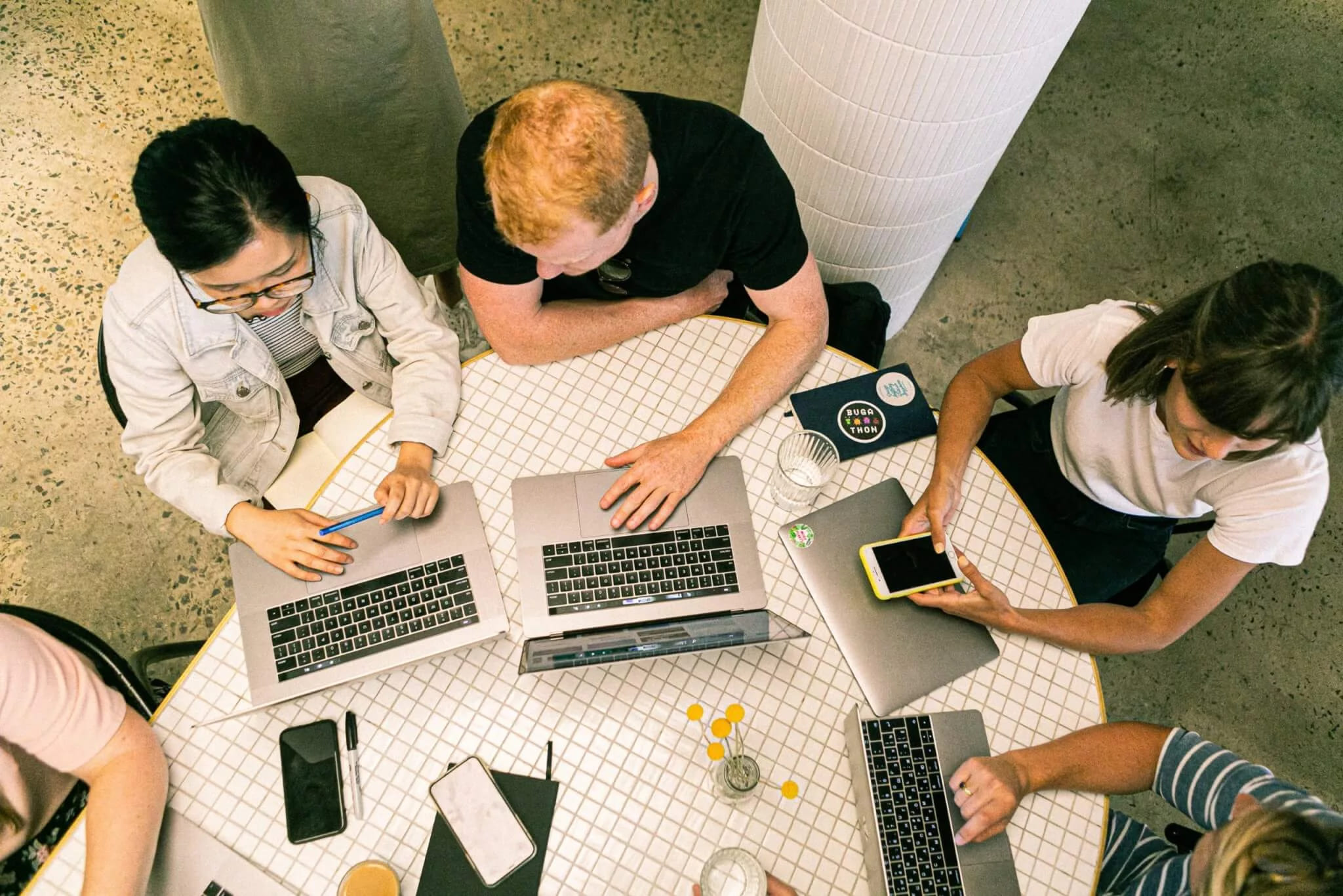 Four people working on laptops around a table, seen from above