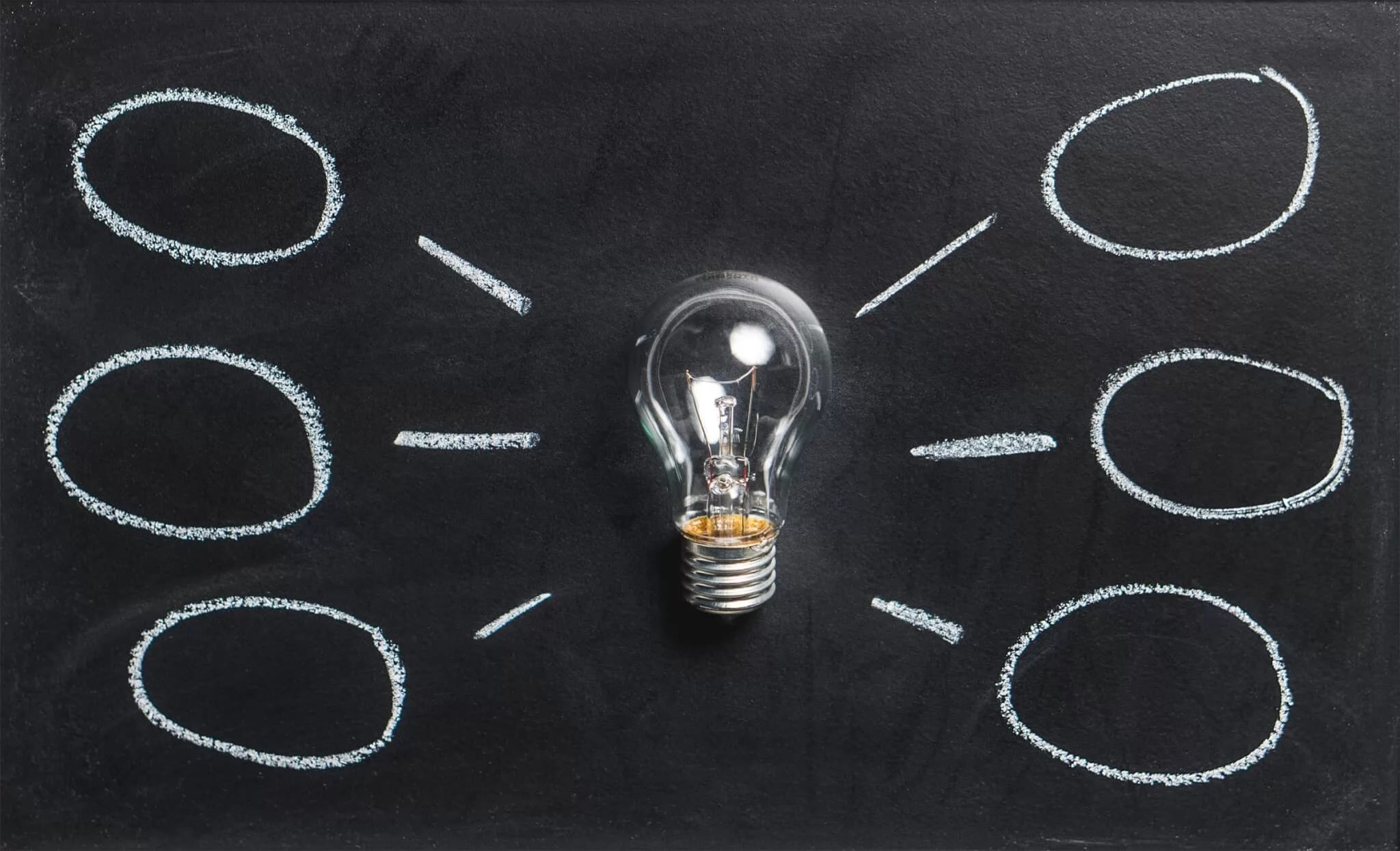 A real bulb lying on a chalkboard among chalk-drawn ovals and dashes