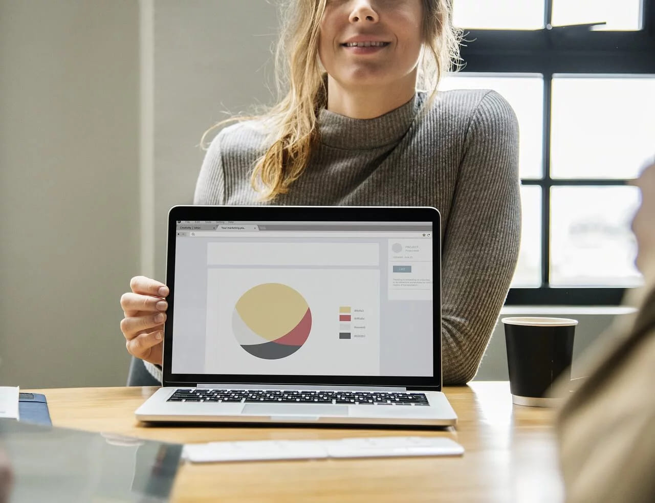 A woman turning her laptop around to show a colleague a pie chart from a marketing plan