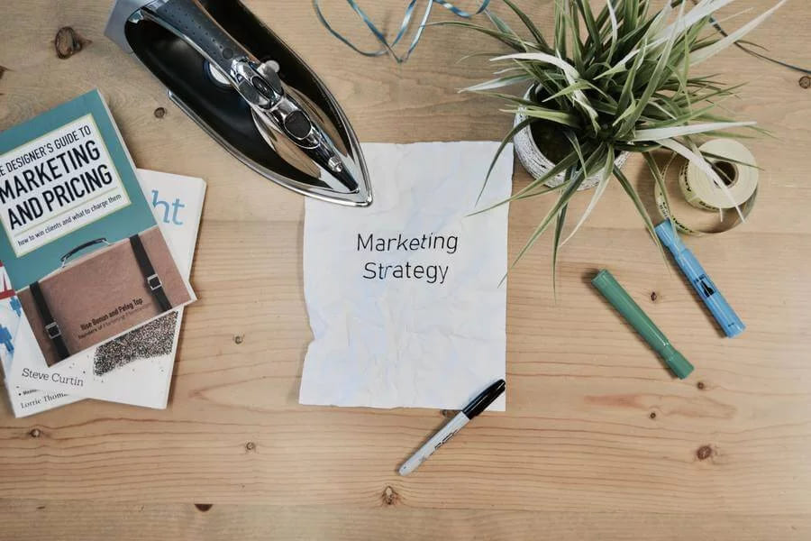 A sheet reading marketing strategy on a desk beside a marketing guide, pens and a plant