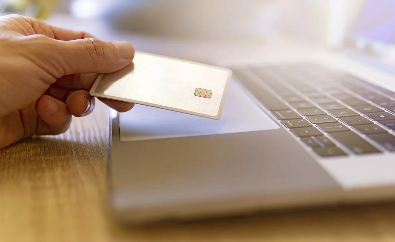 A hand holding a chip bank card in front of an open laptop