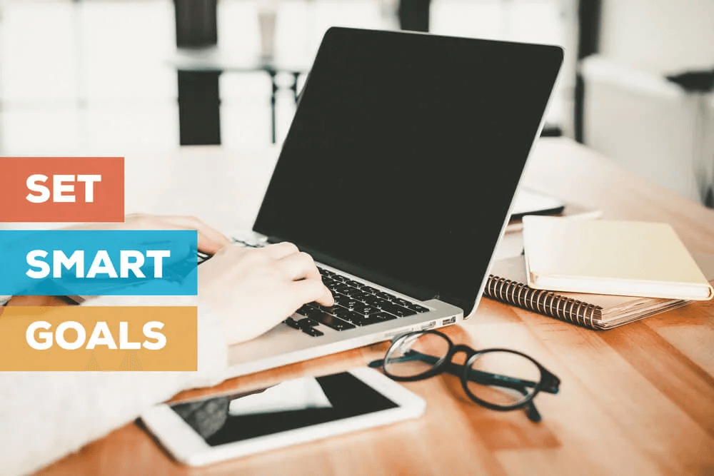 Hands on a laptop beside blocks reading set smart goals, with glasses and a notebook nearby