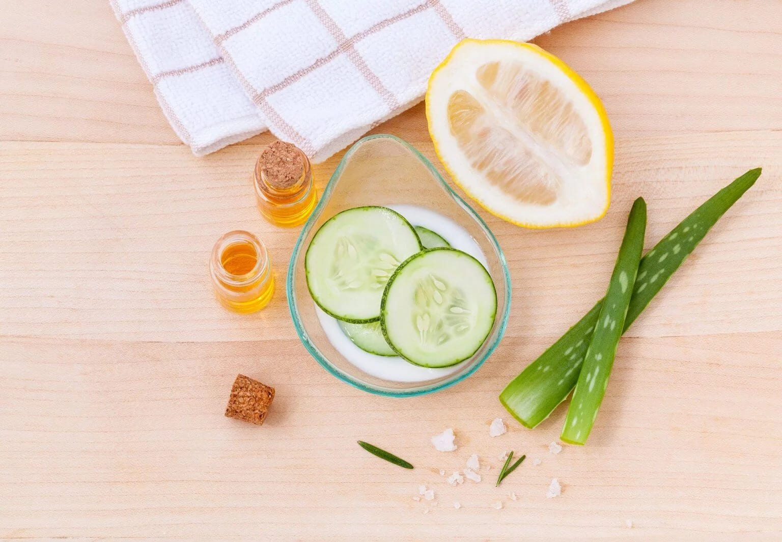 Lemon slices, cucumber, aloe leaves and small jars of cosmetic liquid on a table