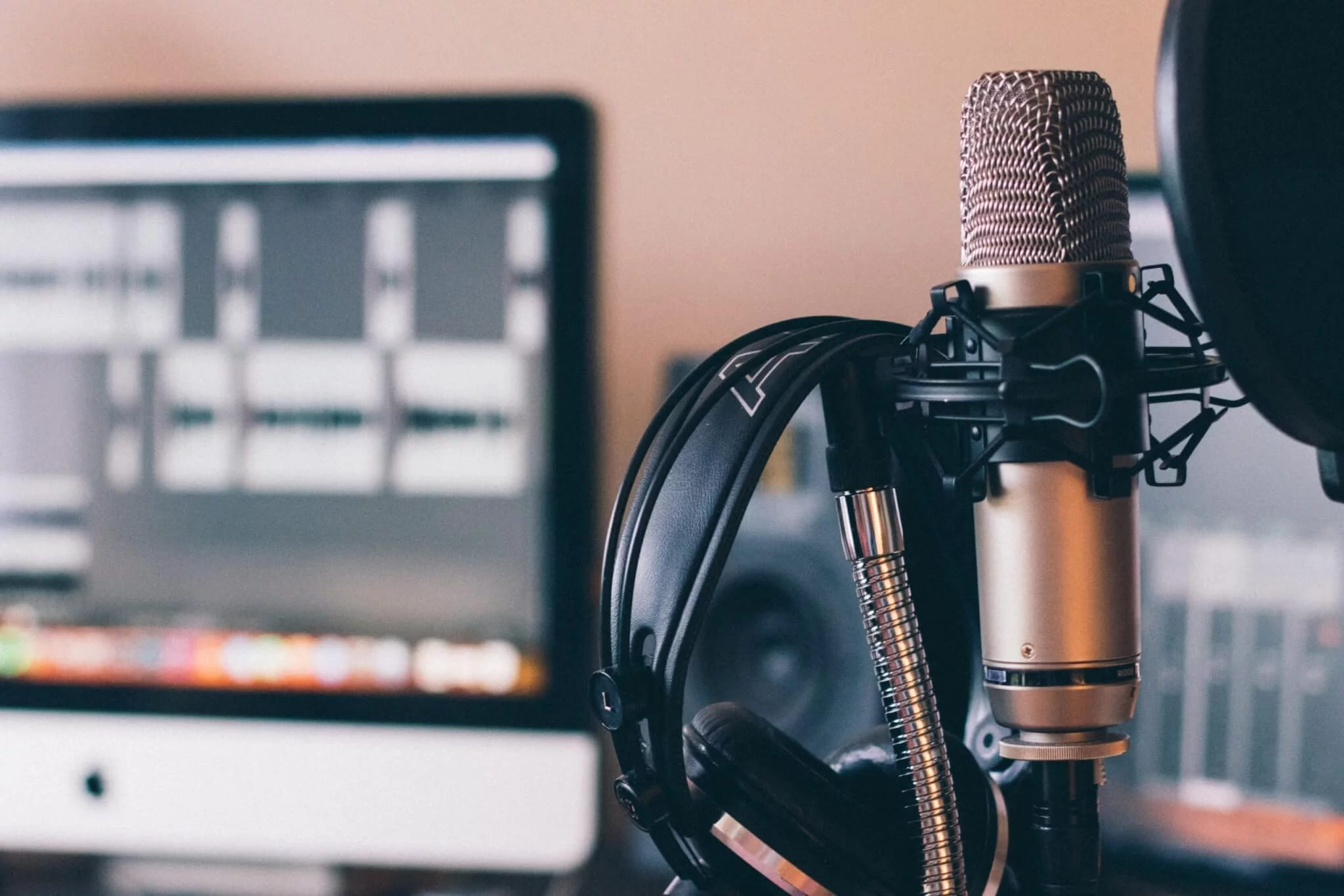 A studio microphone on a stand in front of a monitor with an audio editing timeline